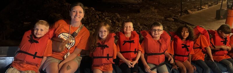 Kids and a teacher in life vests on a boat in a cave.